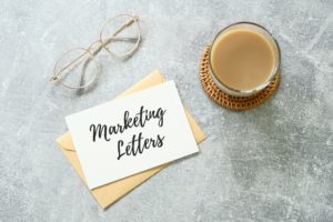 Marketing letters written on paper on top of envelop and next to coffee and glasses